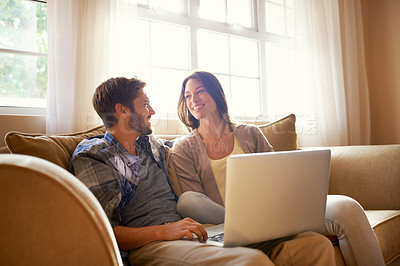 Buy stock photo Shot of a happy young couple using a laptop while sitting on the sofa