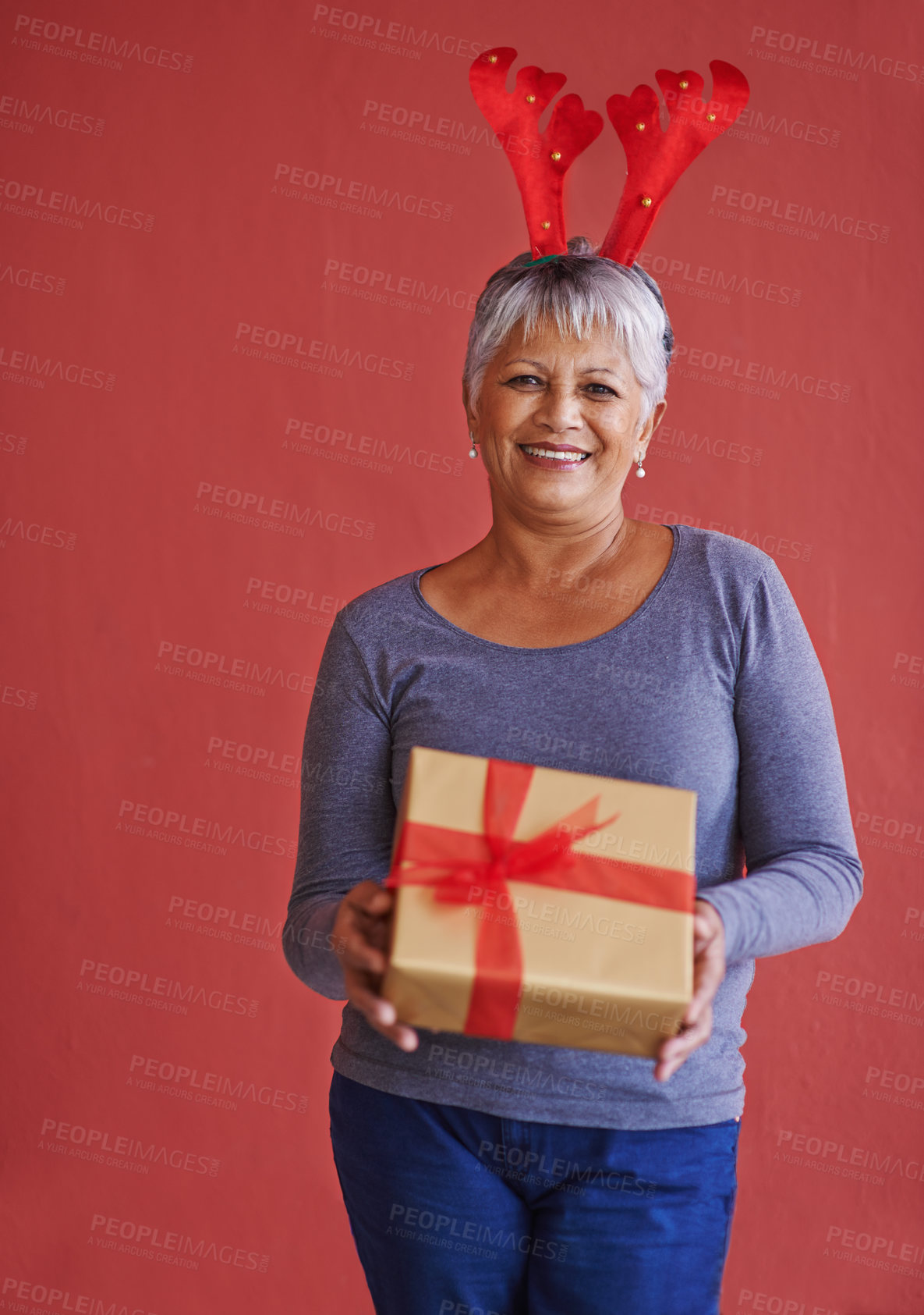 Buy stock photo Shot of a mature woman holding a gift and wearing festive reindeer antlers