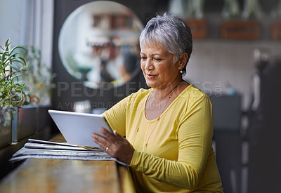 Buy stock photo Shot of a mature woman using a digital tablet in a coffee shop