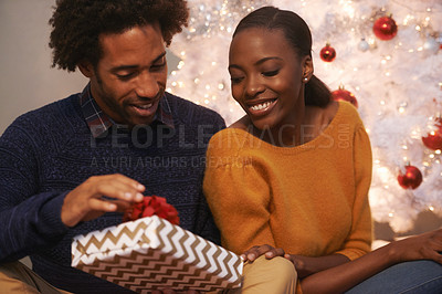 Buy stock photo Shot of a loving young couple unwrapping gifts on Christmas