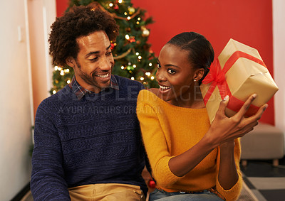 Buy stock photo Shot of a young woman holding up her Christmas present while sitting beside her boyfriend