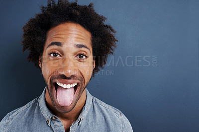 Buy stock photo Portrait of a happy young man sticking his tongue out on a gray background