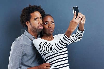 Buy stock photo Love, funny face and couple with selfie in studio for silly, joke or bonding on grey background. Smartphone, app or goofy people hug for blog photography, profile picture or social media comic memory
