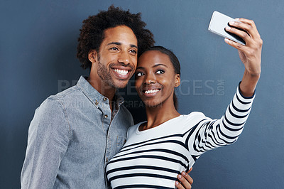 Buy stock photo Shot of a happy young couple taking a photo of themselves with a cellphone on a gray background