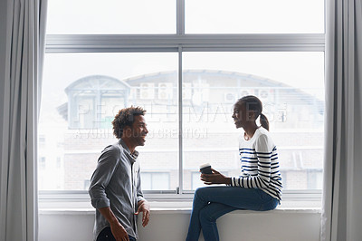 Buy stock photo A happy young couple laughing and chatting next to a large window