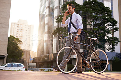 Buy stock photo Shot of a businessman taking a phone call while commuting to work with his bicycle