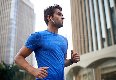 Buy stock photo Shot of a young man jogging through the city