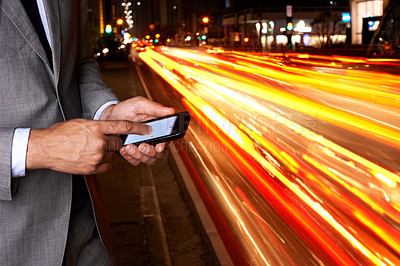 Buy stock photo A cropped shot of a businessman texting while standing beside a busy road