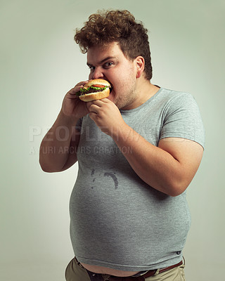 Buy stock photo Obesity, weight gain and hamburger for man in studio with food for unhealthy eating, plus size and greed. Overweight person with meal in mouth and fat stomach for expression humor and comedy indoor