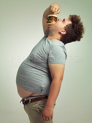 Buy stock photo Fast food, hungry and man with hamburger in studio background with lunch, snack and craving for plus size guy. Male person, burger and takeaway for meal in mouth for eating, starving and bite