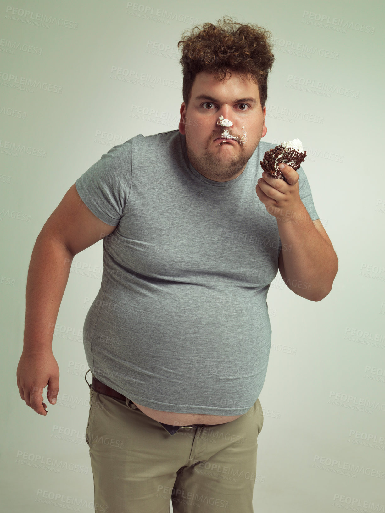 Buy stock photo Plus size, eating and portrait of man with cake in studio for unhealthy, sugar and sweet snack. Greedy, food and male person with messy slice of chocolate dessert isolated by gray background.