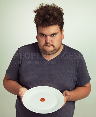 Buy stock photo Portrait, diet or plate and plus size man in studio on gray background, unhappy with size of meal. Food, health or nutrition and disappointed young person frustrated with tiny tomato slice serving