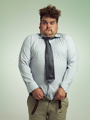 Buy stock photo Man, portrait and shocked with plus size pants or big waist in obesity, overweight or measurement on a studio background. Young male person struggling to fit clothing with body fat or chubby stomach