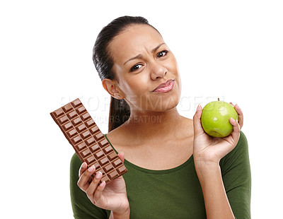 Buy stock photo Portrait of a young woman trying to decide between chocolate and an apple isolated on white