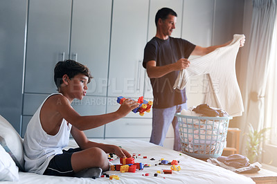 Buy stock photo Cropped shot of a young boy playing with toys while his father folds laundry in the background
