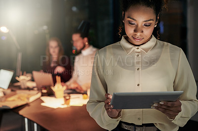 Buy stock photo Shot of an attractive young designer working late at the office with her colleagues in the background