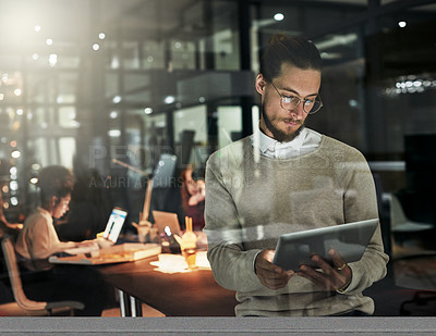 Buy stock photo Shot of a handsome young designer working late at the office with his colleagues in the background