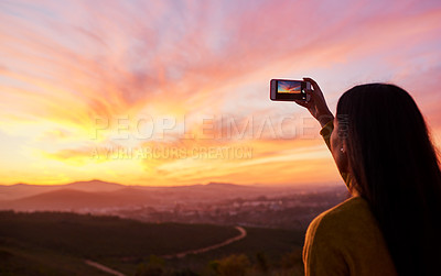 Buy stock photo Rearview shot of a woman taking a photo of a sunset with her smartphone