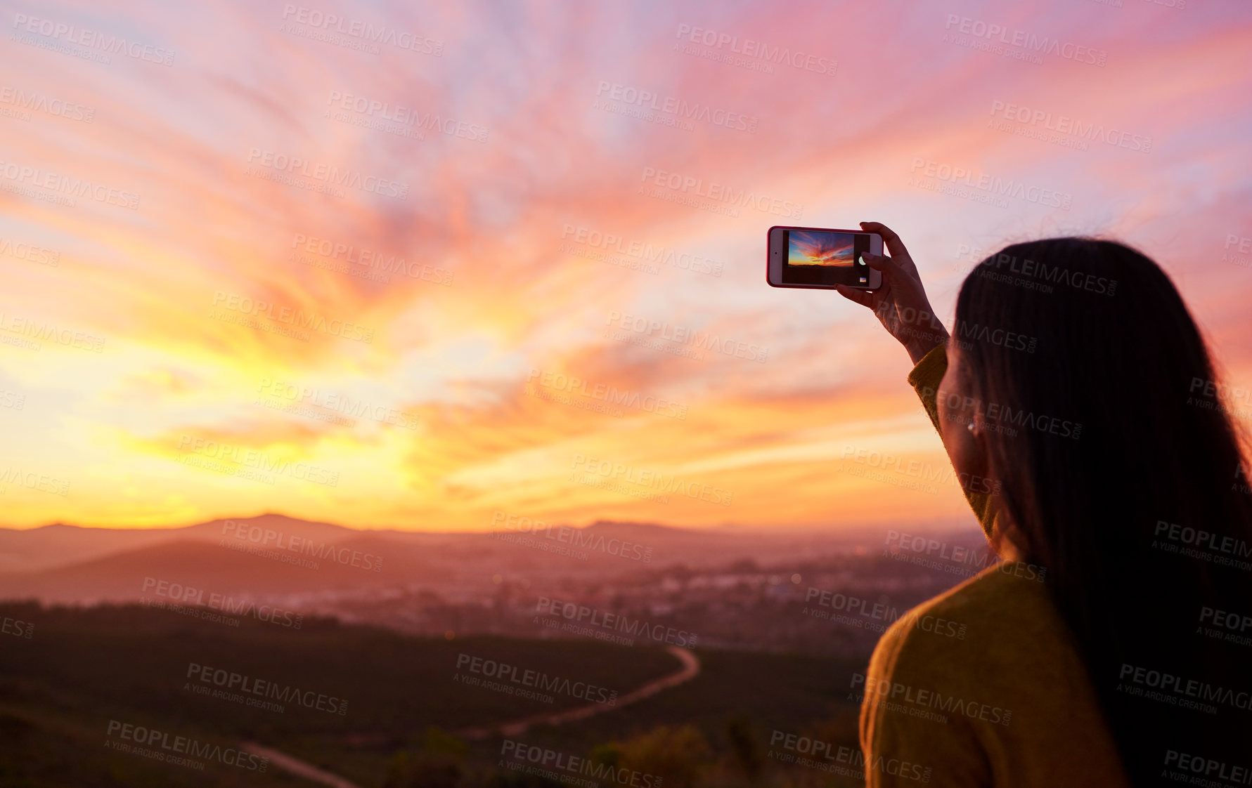 Buy stock photo Rearview shot of a woman taking a photo of a sunset with her smartphone