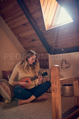 Buy stock photo Shot of a young woman playing the ukelele while relaxing in her bedroom at home