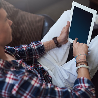 Buy stock photo High angle shot of a young man using his tablet while sitting on the sofa at home
