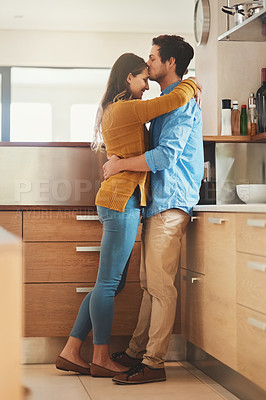Buy stock photo Shot of an affectionate young man kissing his girlfriend on the forehead in their kitchen
