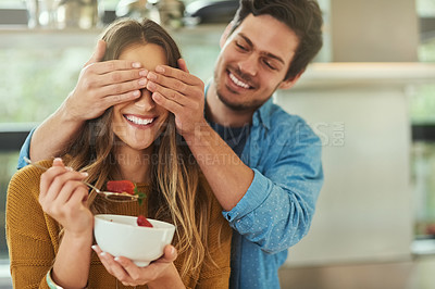 Buy stock photo Shot of an affectionate young man covering his girlfriend's eyes while she eats breakfast in their kitchen