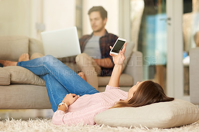 Buy stock photo Shot of a happy young couple using there wireless devices from the comfort of their lounge