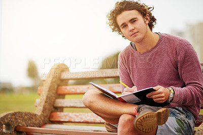 Buy stock photo Portrait of a young man sitting on a park bench writing in a notebook