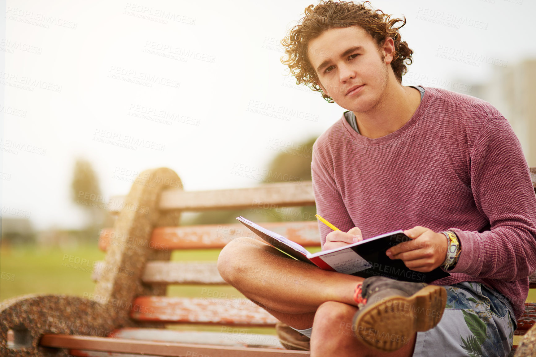 Buy stock photo Portrait of a young man sitting on a park bench writing in a notebook