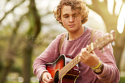 Buy stock photo Shot of a young man playing guitar outside