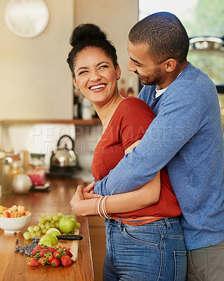 Buy stock photo Shot of a young man hugging his wife while she prepares a healthy snack at home