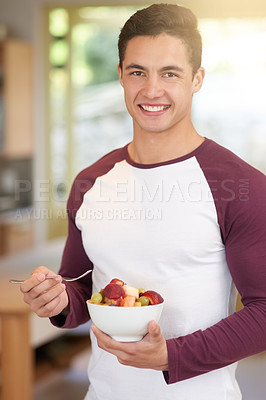 Buy stock photo Portrait of a happy young man enjoying a healthy breakfast of fruit in his kitchen at home