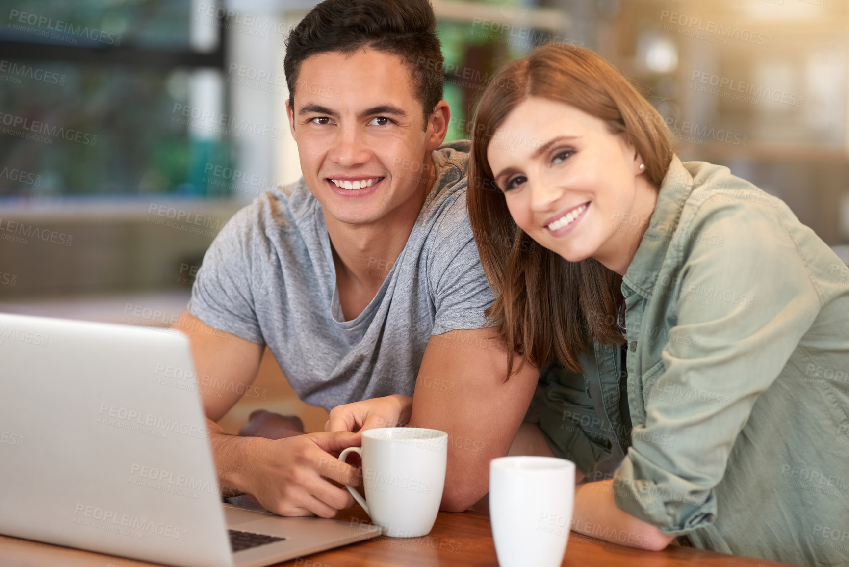 Buy stock photo Portrait of a happy young couple using their laptop while having coffee in their kitchen at home