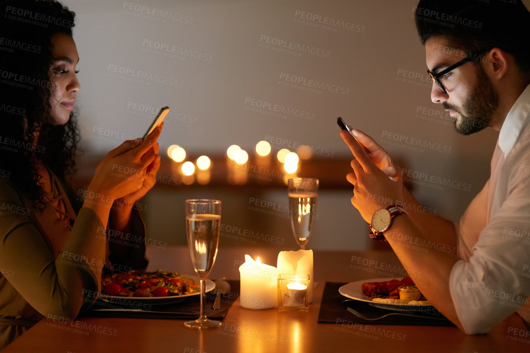 Buy stock photo Shot of a young couple texting on their phones while out for dinner