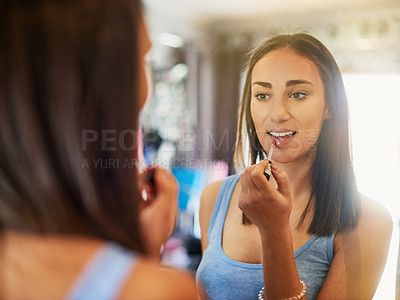 Buy stock photo Shot of an attractive young woman applying lipgloss in a mirror at home