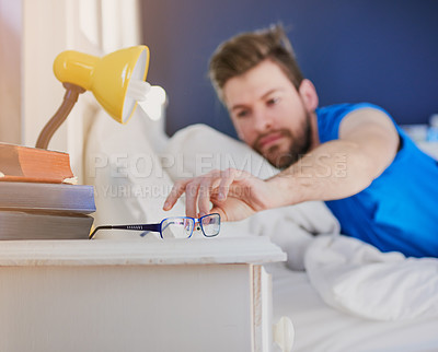 Buy stock photo Cropped shot of a young man reaching for his spectacles after waking up from bed