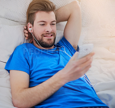 Buy stock photo Cropped shot of a handsome young man listening to music while lying on his bed at home