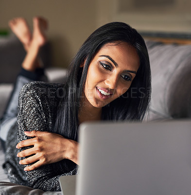 Buy stock photo Shot of an attractive young woman surfing the net while lying on her sofa at home