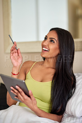 Buy stock photo Shot of a thoughtful young woman using a digital tablet in bed