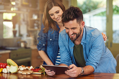 Buy stock photo Shot of a happy young couple using a digital tablet while preparing a healthy meal together at home
