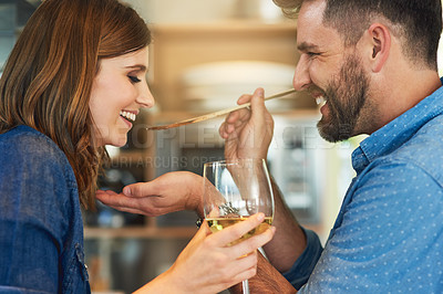 Buy stock photo Shot of a man giving his wife a taste of the food that he’s preparing at home
