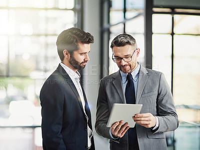 Buy stock photo Shot of two businessmen looking over a tablet in the office