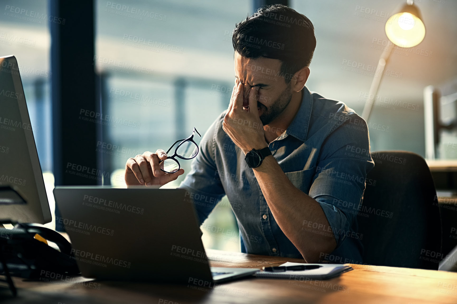 Buy stock photo Shot of a young businessman experiencing stress during a late night at work