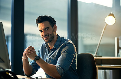 Buy stock photo Portrait of a young businessman on a computer during a late night at work. Confident hardworking man at a corporate office desk working overtime, dedicated and committed alone at the workplace.