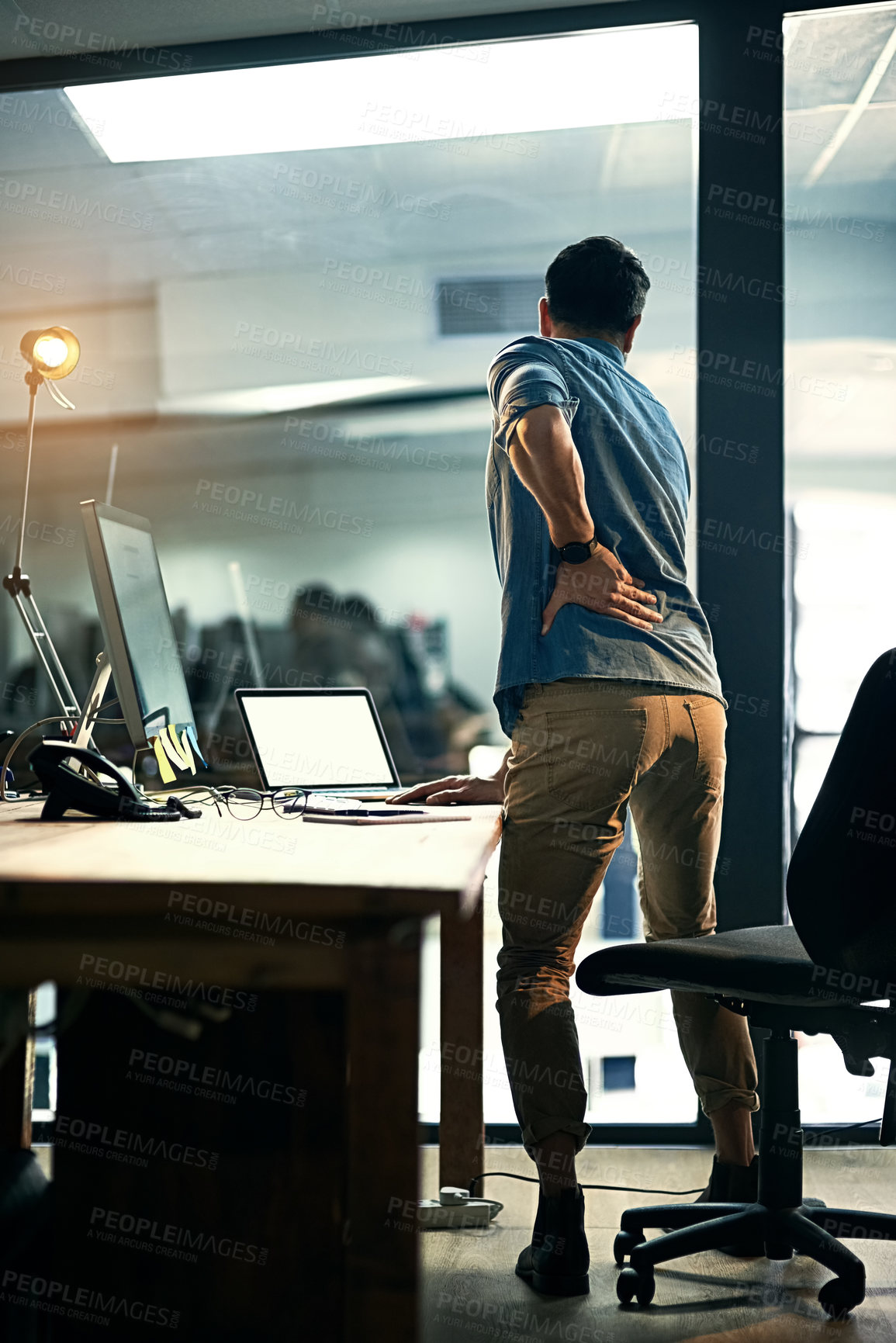 Buy stock photo Rearview shot of a businessman suffering from backache while working at night