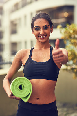 Buy stock photo Shot of a young woman showing thumbs up while holding her yoga mat