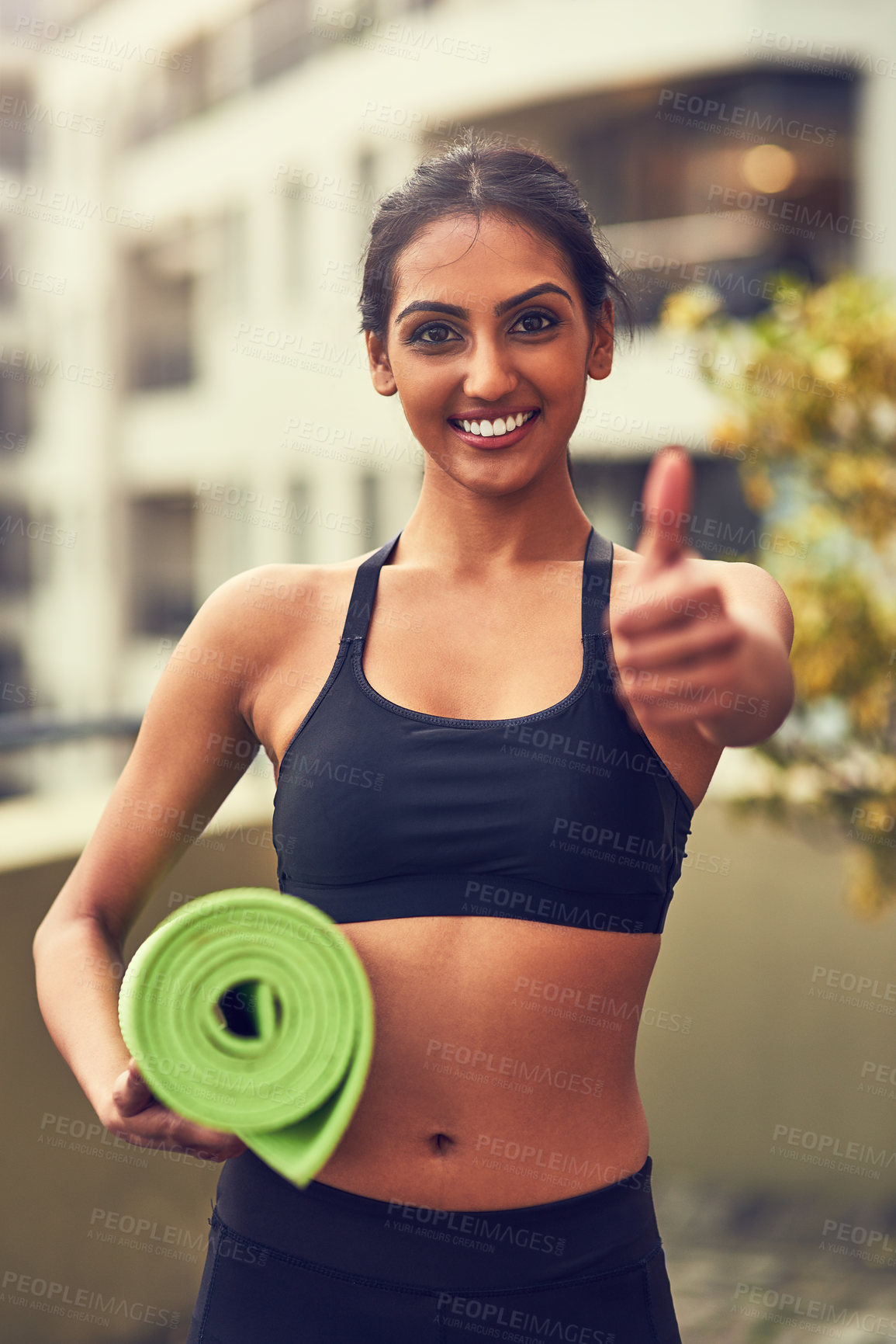Buy stock photo Shot of a young woman showing thumbs up while holding her yoga mat