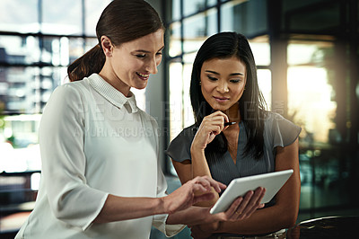 Buy stock photo Shot of two young businesswomen looking over a tablet in the office