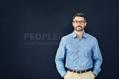 Buy stock photo Studio portrait of a handsome businessman standing with his hands in his pockets against a dark background